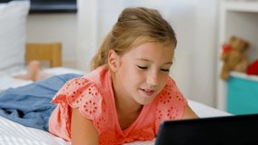 children, technology and communication concept - smiling girl having vide call on tablet computer lying on bed at home