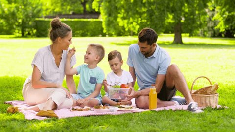 family, leisure and people concept - happy mother, father and two little sons eating fruits on picnic at summer park