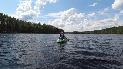 A female paddling a green inflatable kayak on a small lake. Filmed from behind at half speed.