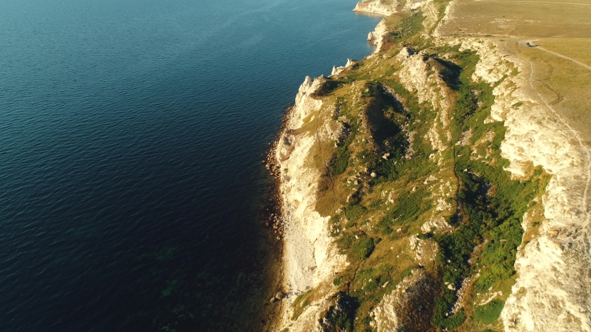Aerial view of picturesque long white cliff covered with green grass, trees and shrubs near the sea at warm summer day. Shot. Beautiful landscape of cliff and seashore
