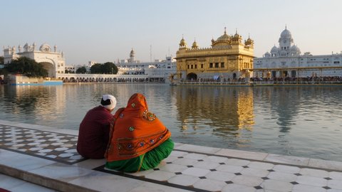 a wide shot of two sikh worshipers sitting beside the pool at the famous golden temple in amritsar, india- 4K 60p