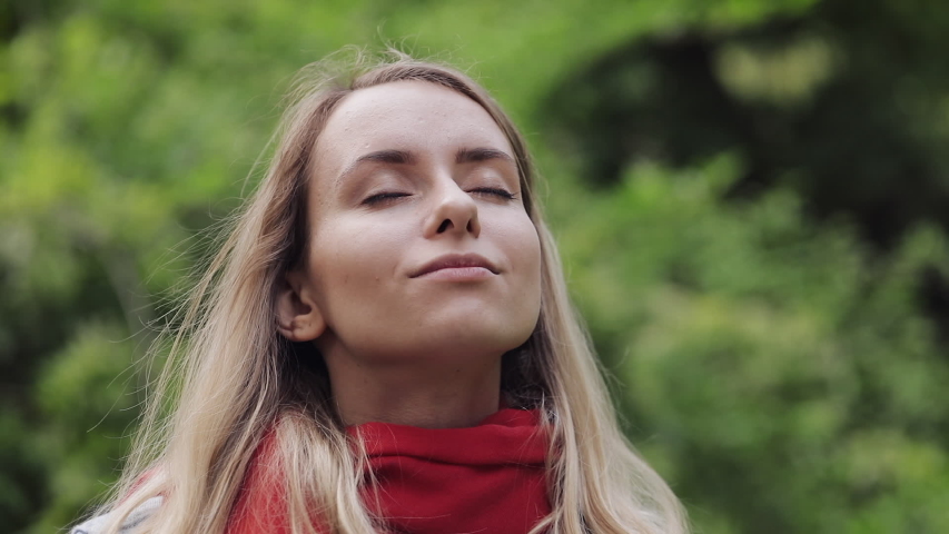 Portrait of Young Beautiful Woman Wearing Red Scarf Inhaling and Exhaling Fresh Air, Taking Deep Breath, Reducing Stress and Looking into the Camera. She is Smiling. Healthy Lifestyle Concept.