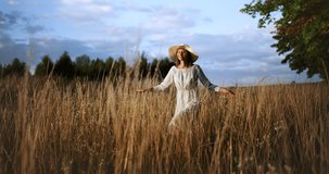 Attractive young stylish lady walking on field and holding hat, feeling happy and inspired