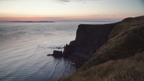 View over the edge of the Cliffs of Moher in Ireland to a silhouetted rock face against a beautiful sunset