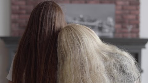 Back view of two girls with long beautiful hair sitting near each other in the living room. Concept of friendship. Carefree childhood. Contrast appearance