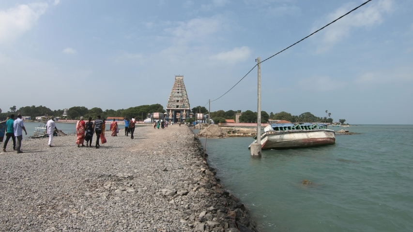 People go to ancient hindu temple Nainativu Nagapooshani Amman Kovil gopuram big colorful tower broken boat near pier green island Jaffna Sri-Lanka