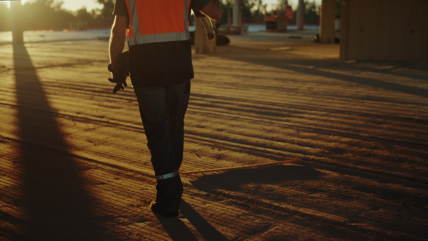 Inside of the Commercial / Industrial Building Construction Site: Professional Engineer Surveyor Finishes Day's Job Carries Tripod Theodolite and Walks into the Sunset Royalty-Free Stock Footage #1034288147