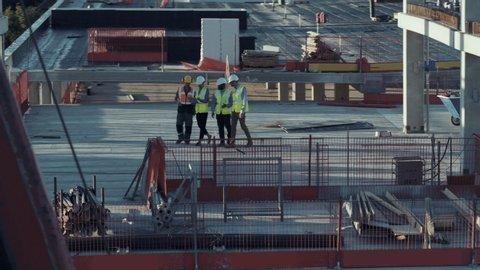 Aerial View: Diverse Team of Specialists Talking On the Roof Commercial, Industrial Building / Skyscraper Formwork Construction Site. Real Estate Project Civil Engineer, Investor, Architect and Worker