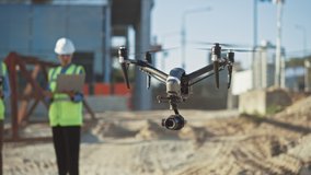 Two Specialists Use Drone on Construction Site. Architectural Engineer and Safety Engineering Inspector Fly Drone on Commercial Building Construction Site Controlling Design and Quality.Focus on Drone - Powered by Shutterstock - Get 15% off with code: PIKWIZARD15