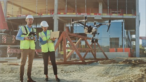 Two Specialists Using Drone on a Construction Site. Architectural Engineer and Safety Engineering Inspector Fly Drone on Commercial Building Construction Site Technical Control of Design and Quality