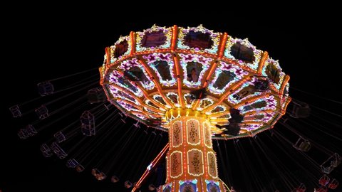 Low angle view of colourful illuminating moving and spinning swing ride or swing carousel on background of night dark sky at Rheinkirmes Carnival in Düsseldorf, Germany.