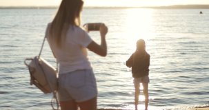 Mom takes pictures of her daughter on the background of the sunset. Cute girl dancing by the lake. Sun kissed child.