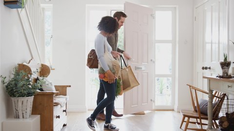Couple Returning Home From Shopping Trip Carrying Groceries In Plastic Free Bags