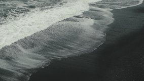 Aerial of waves crashing on a black sand beach (Reynisfjara) in Iceland. Slow motion. Color graded.