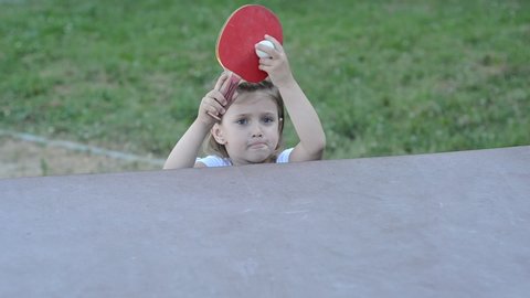 Little charming happy girl child plays ping pong on the street	