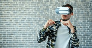 Portrait of man in vr glasses boxing moving hands on brick wall background enjoying digital sports. Modern gadgets, young people and entertainment concept.
