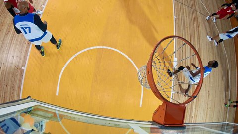High angle of professional basketball player in action performing slam dun in a basketball hoop on a sports arena
