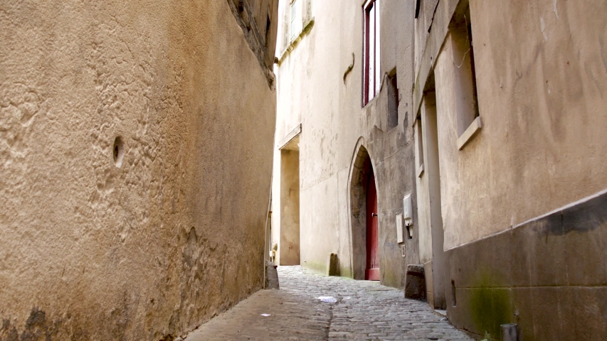 Mysterious side alley. It is a cobbled road. Houses either side with red door in shot.