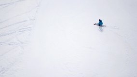 Aerial - Top view tracking shot of good alpine skier skiing down the wide ski slope alone. Sunny winter day in Austrian mountains