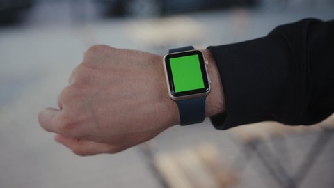 Male hand in horizontal position showing modern smartwatch gadget with chrome key green mockup screen. Guy using innovative wrist watch staying in the city street.