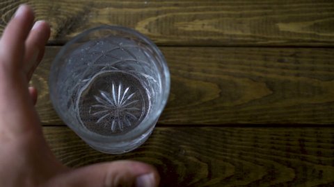 Slow motion shot of a male bartender placing down an alcoholic drink on a wooden table and dropping a lemon into it.