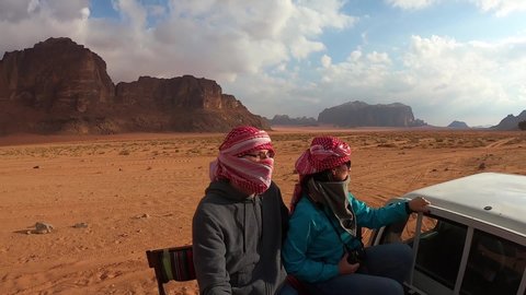 Wadi Rum, Jordan - November 14 2018: Young tourist couple having a Jeep desert tour around Wadi Rum desert, being driven by an old jeep and overlooking Orange colored landscape.