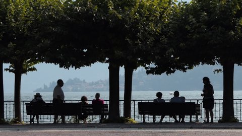 Cernobbio, July, 2019 – group of elderly people rest and talk sitting on the benches by the lake