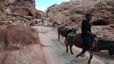 Petra, Jordan - November 14 2018: Local Bedouin people riding donkeys through the ancient city of Petra on narrow stone steps and waving to the camera.