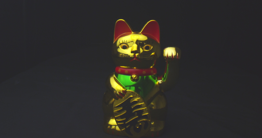 Closeup shoot of golden shiny chinese lucky cat waving a paw with background isolated on black