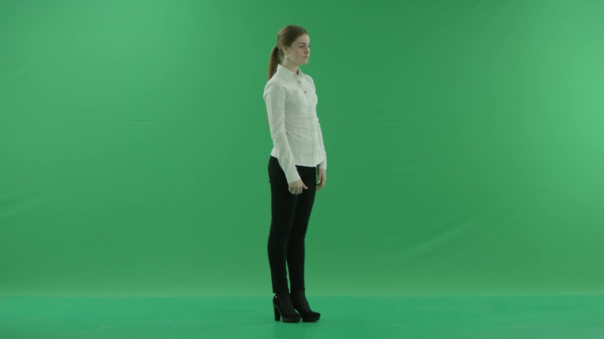 surprised excited woman is laughing and giving a thumbs-up. She wears formal dress: white shirt and blak trousers. Lady stands sideways in the centre of a green screen