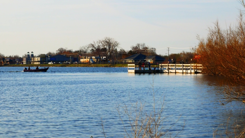 People in a fishing boat and on a pier on Lake Bemidji near the Mississippi River on the morning of Minnesota Fishing Opener with buildings and traffic on far shore.
