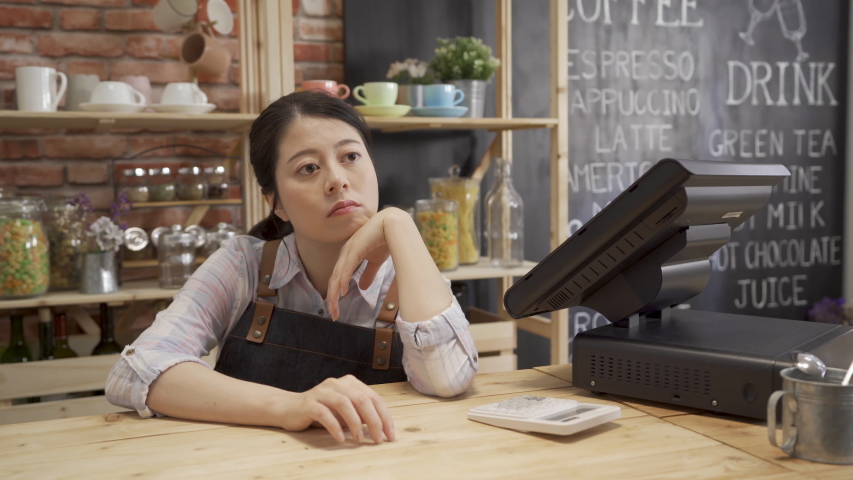 small startup business owner depressed while economy in slump. cafe store waitress with hand on chin in counter using finger drumming on wood table. bored barista waiting for customer in coffee shop. Royalty-Free Stock Footage #1034346467