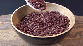 Red beans falling into a wooden bowl. Wooden background. Closeup. Food video. Uncooked beans Raw cereal falling into beautiful dishes Macro slow motion. 