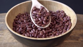 Red beans falling into a wooden bowl. Wooden background. Closeup. Food video. Uncooked beans Raw cereal falling into beautiful dishes Macro
