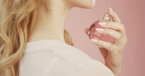 Beautiful cute tender young girl with nude makeup holds bottle of perfume with pink liquid, in studio on pink background. Concept for advertising perfume. Gentle makeup and developing hair.