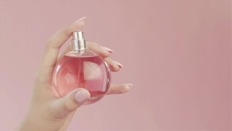 Beautiful tender graceful hand of girl with pink nails and long fingers, spray from  bottle of perfume with pink liquid in studio on pink background. Concept for advertising perfume.