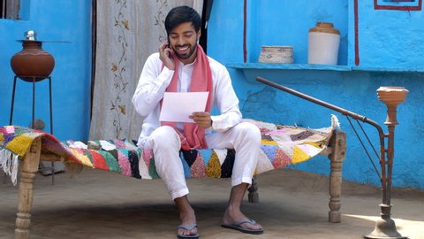 Happy Indian man received money and a letter of appreciation - financial concept. Rural home. Young attractive villager is smiling after receiving money and confirmation letter from government sche...