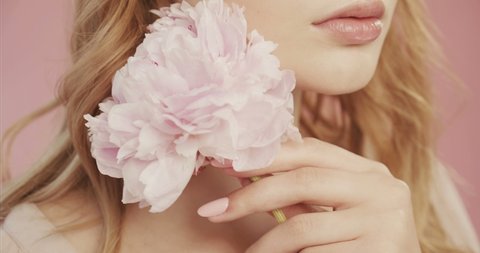 Beautiful lovely girl with nude makeup holds magnificent pink color of peony close to face. In the studio on pink background. Delicate makeup, expressive eyes. Concept for perfume and cosmetics.