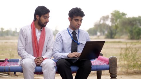 Young government employee explaining new agricultural policies to an illiterate farmer . Indian government official in formals sitting with young farmer, showing him new agricultural techniques an...
