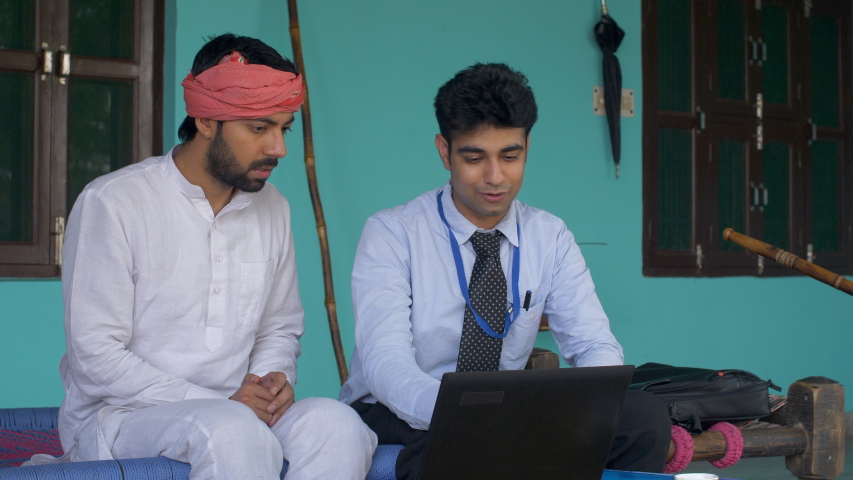 Young bank employee congratulating innocent Indian villager on his loan approval. Happy Indian farmer with a loan agent. Applying for tractor loan - village scene Royalty-Free Stock Footage #1034355080