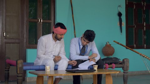 Young attractive bank agent guiding Indian farmer to fill-up new bank account's form . Handsome bank agent helping village man for saving account form - Financial Inclusion