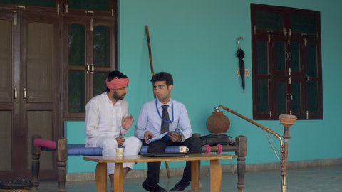 Young attractive dealer with an Indian villager - Discussing some legal documents. Indian village home setup - A man dressed in formals is explaining loan formalities to the farmer. Hukka and Matka...