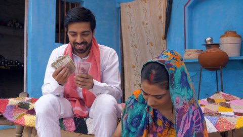 Young good looking village husband giving Indian rupee notes to his wife - future investment . Indian villager happily giving his monthly salary to his beautiful wife - village life in India