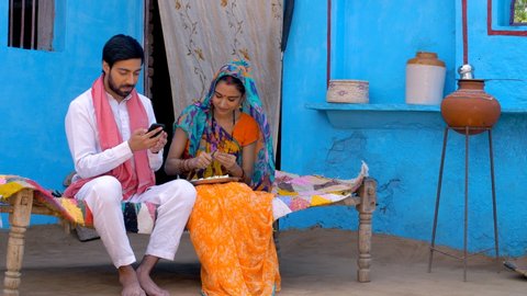 Young attractive husband showing new things to his beautiful wife on his new smartphone - Village life. Village scene of an Indian farmer and his wife showing new things on his mobile phone, smilin...