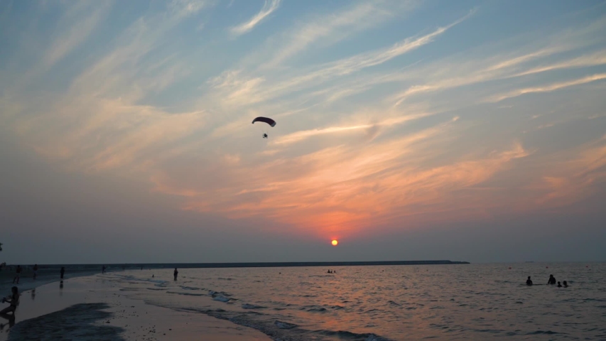 Motor paraglider flying over an Arabian Gulf beach on an astonishing orange sunset.
