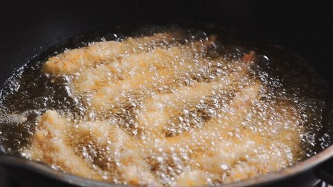 Close up of chef using metal tongs to flip deep fried shrimp in pan with boiling oil