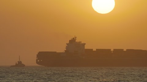 Silhouette of a large cargo ship quickly moving across the ocean as the sun sets