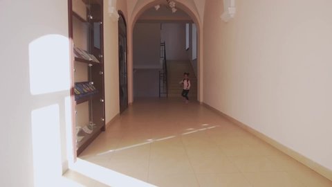 Front view of little african girl with backpack running in corridor in school. Funny child looking at camera, laughing and resting after lessons. Concept of childhood and happiness.