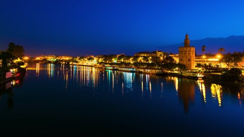 Seville, Spain. View of La Torre de Oro Tower of Gold in Seville, Spain at sunrise. Time-lapse with reflection in the Guadalquivir River and clear sky, zoom in