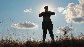 Silhouette: Plus size woman doing sport exercises on grass spending time in highlands in the morning. Slow-motion video